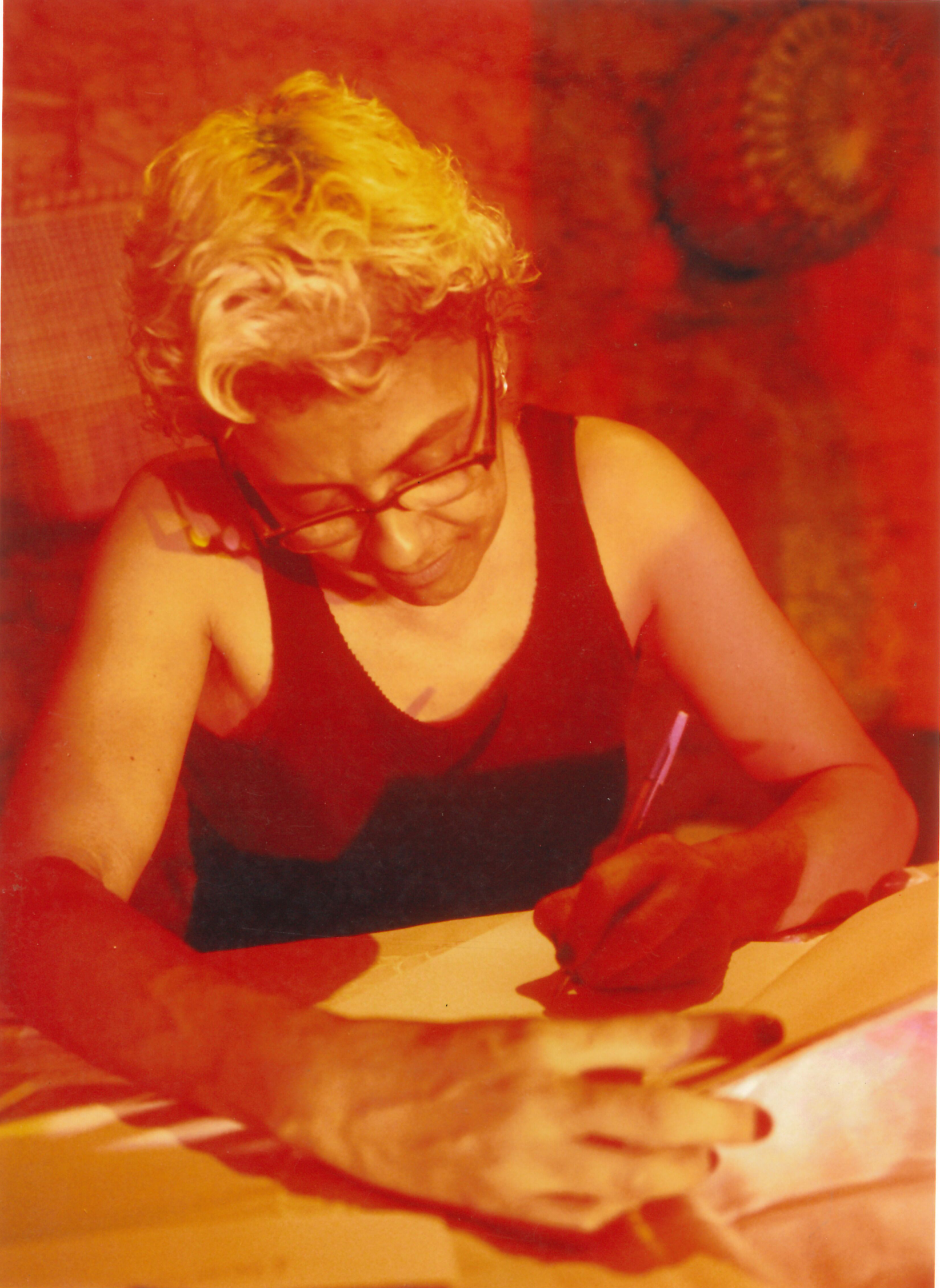 Em uma fotografia em tons de vermelho, Marise autografa o livro, parte do trabalho que estava sendo lançado na ocasião. Junho de 2007, São Luís -MA.