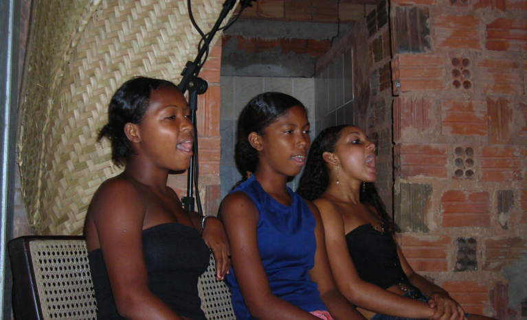 Bandeirinhas são meninas que cantam respondendo em coro ao canto das Caixeiras. 
                  Aqui Daniele de Jesus Leitão, Danielle Rodrigues Pereira e Claudilene Rodrigues Pereira cantam durante as gravações para o projeto de Salvaguarda do repertório musical dos Festejos do Divino em Alcântara, realizado para o Iphan-MA. 
                  Foto de Marise Barbosa 2009.