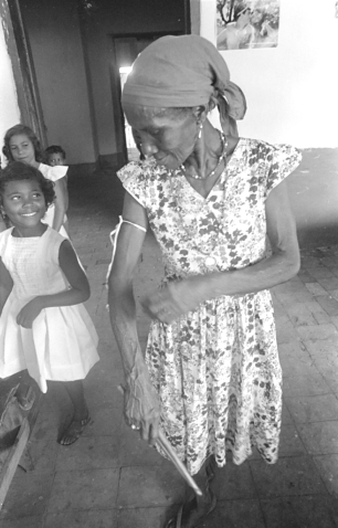 Raimunda Boró antiga e famosa Caixeira em Alcântara, foi presa com um laço em seu braço. Uma brincadeira da qual ela sai quando pessoas suas amigas ou parentes pagarem prendas que pode ser alguma bebida por exemplo. Foto de Juvenal Pereira.  Década de 1980